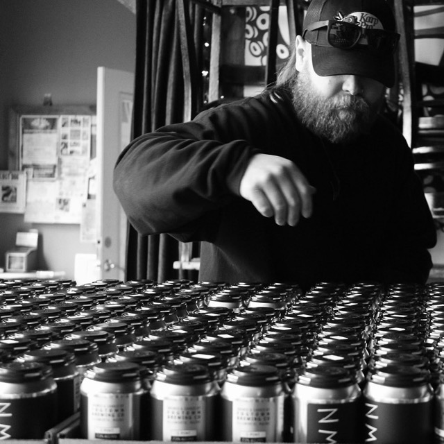 A brewer working over rows of freshly filled cans, in black and white