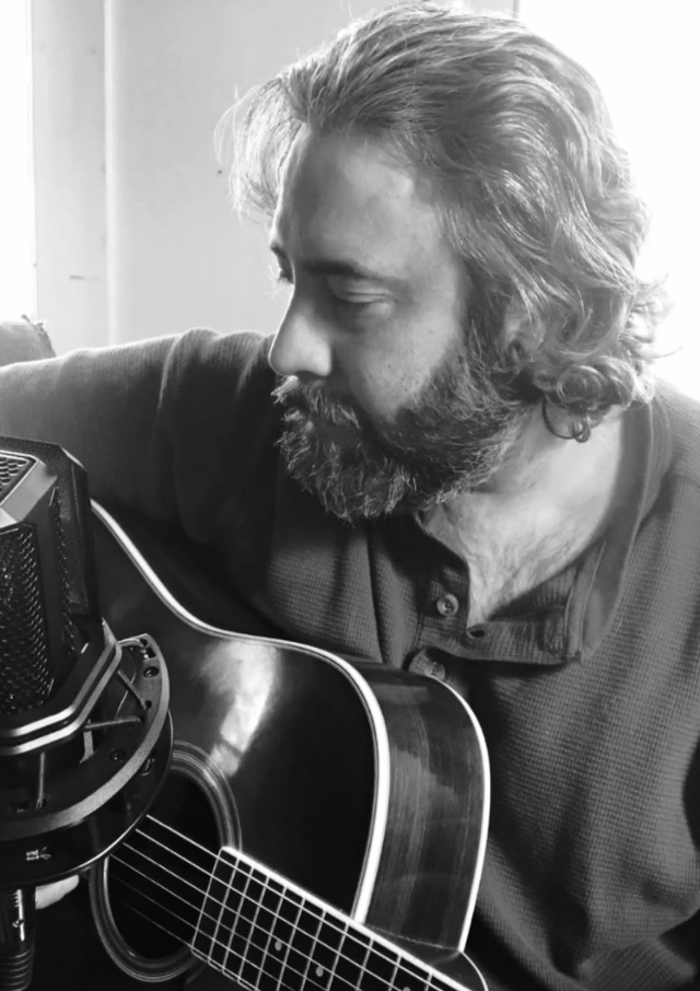 Chris Ross with an acoustic guitar, in black and white