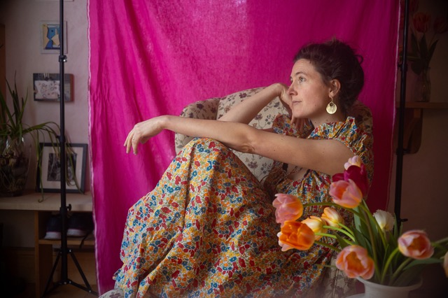 Katherine Perkins seated in front of a pink backdrop with tulips