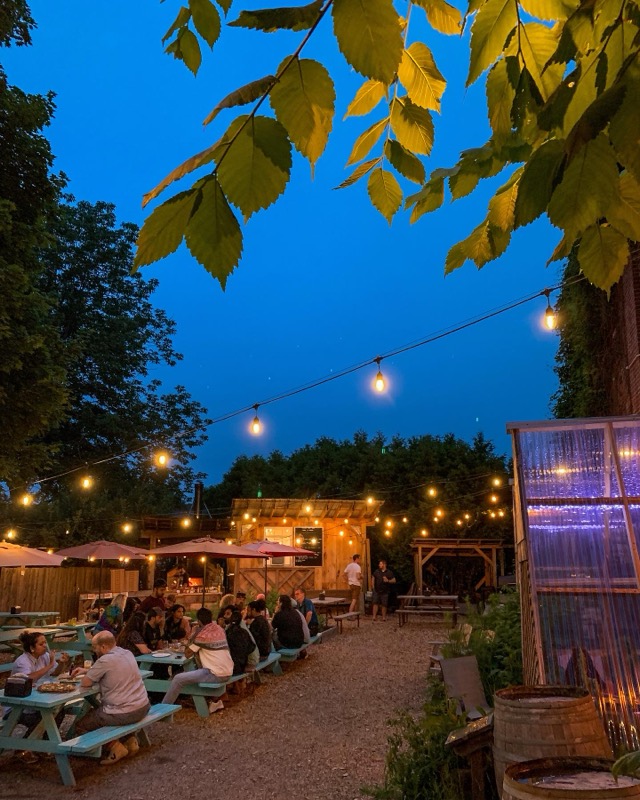 The beer garden at dusk, string lights glowing against a deep blue sky