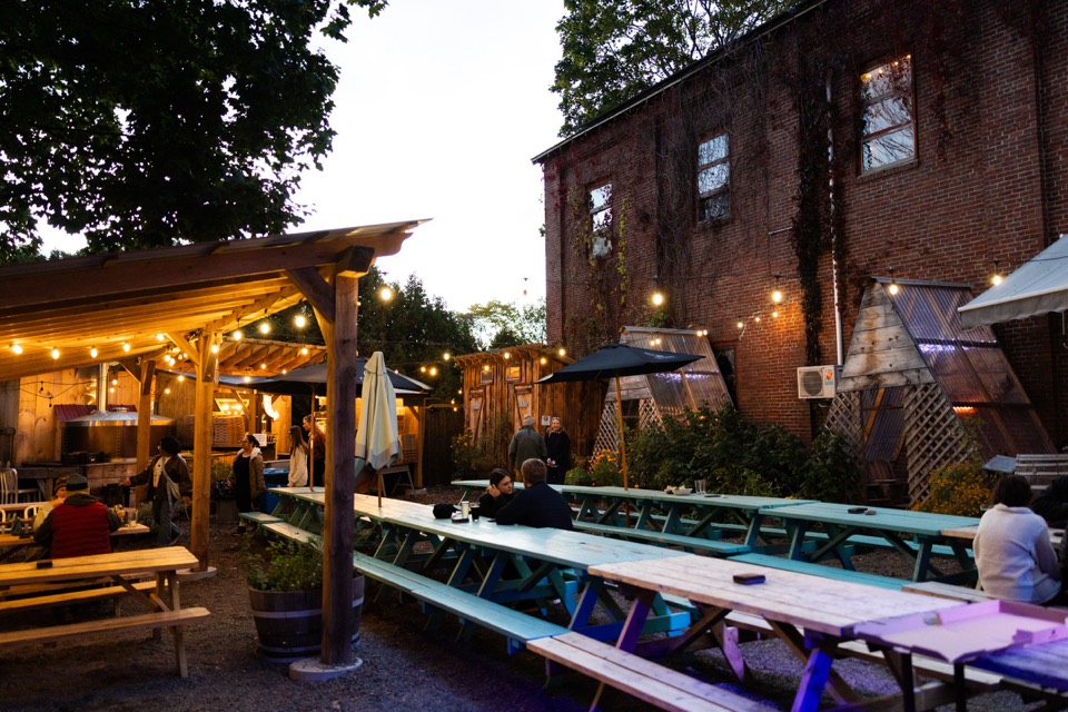 Fogtown’s beer garden at twilight, string lights over long picnic tables beside the brick brewery