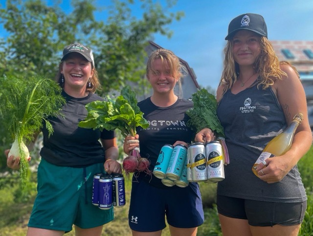 Three friends holding garden greens and four-packs of Fogtown cans