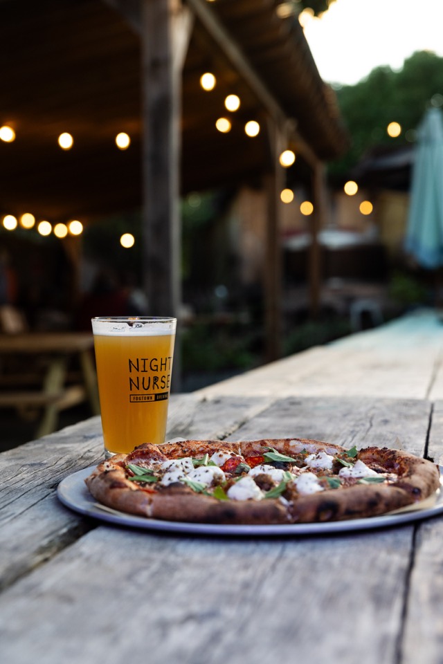 A Night Nurse pint and a pizza on a picnic table under the garden’s string lights