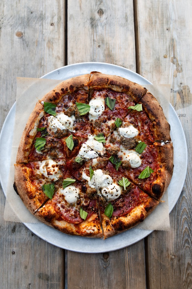 A whole pizza with mozzarella and basil on a weathered wooden table, seen from above