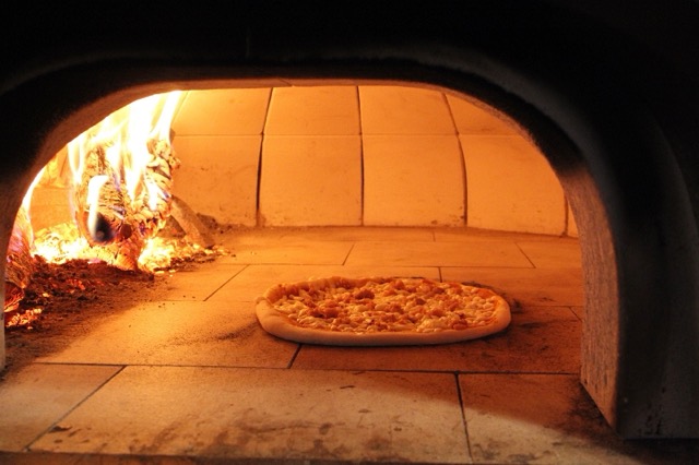Flames at the back of the wood-fired oven with a pizza baking