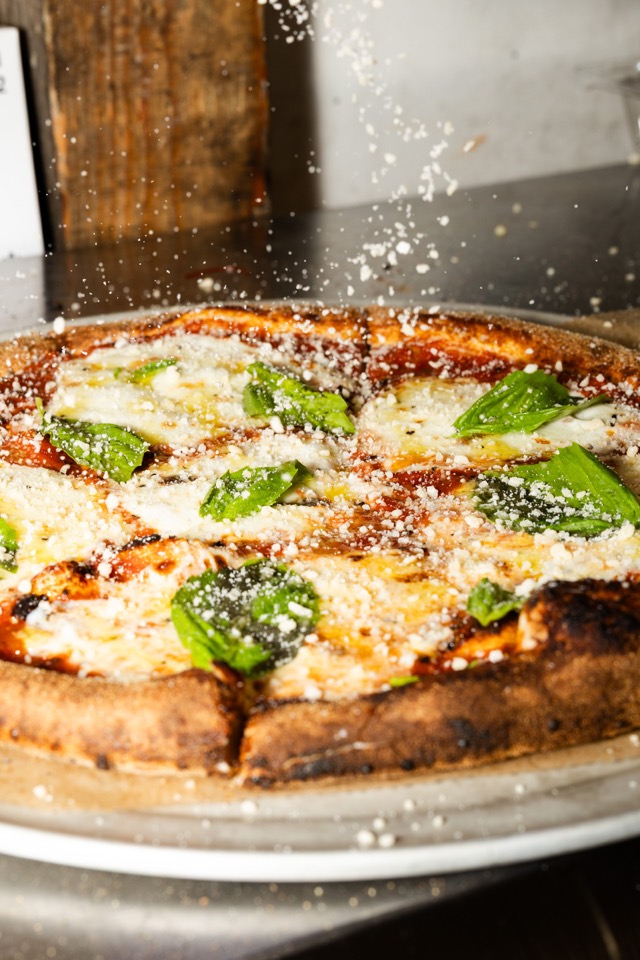 Parmesan falling onto a margherita pizza with basil leaves