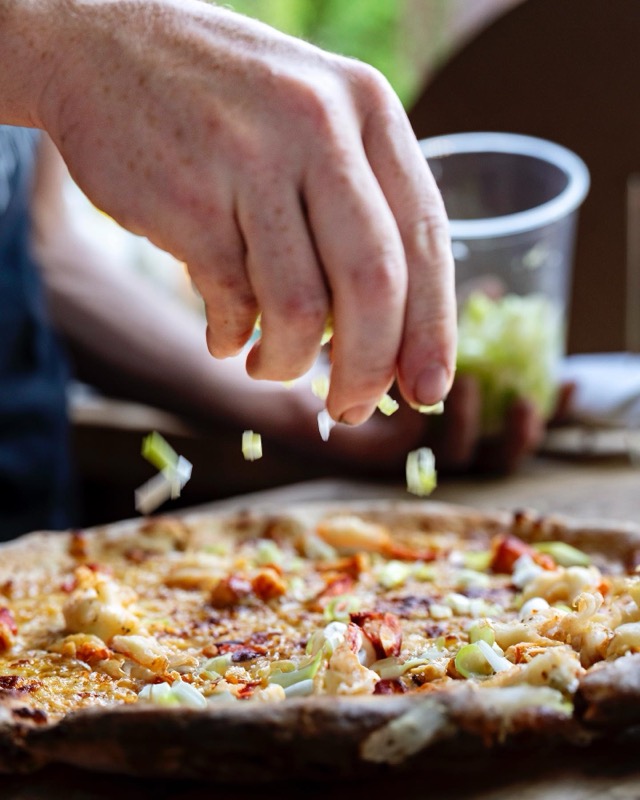 A hand scattering toppings over a pizza